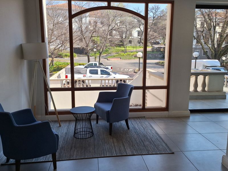 A bright office waiting area featuring large arched windows with views of the exterior, neutral ceramic floor tiles, and a clean, modern aesthetic.