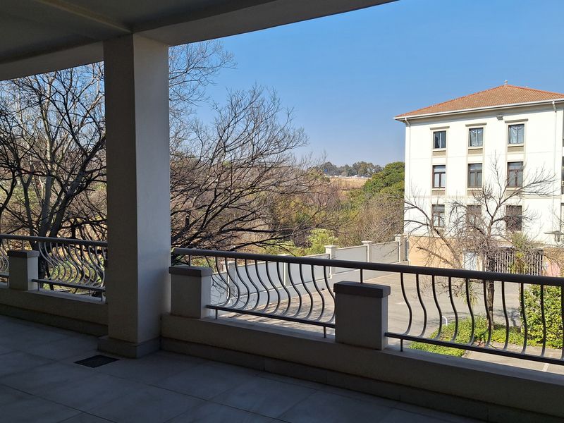 A spacious covered balcony featuring tiled flooring and a decorative metal balustrade, offering an open view of the surrounding office complex and landscape.