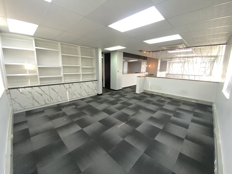 A bright, open-plan office space featuring modern built-in shelving, marble-effect base cabinetry, carpet tiles, and recessed ceiling lighting.