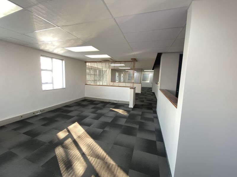 An open-plan office space featuring suspended ceilings, carpet tiles, and a partial partition wall with timber detailing.