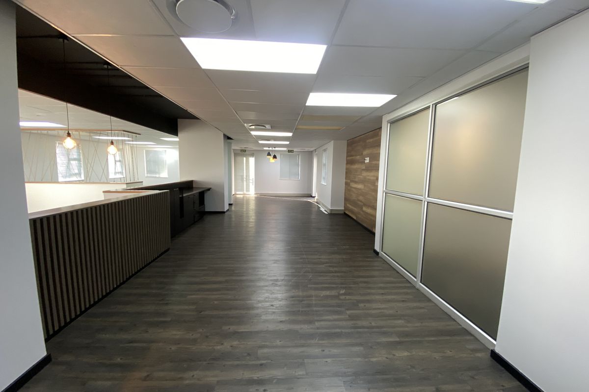 Spacious open-plan office area featuring modern laminate flooring, a wood-paneled feature wall, and frosted glass partitions, offering a clean and professional workspace.