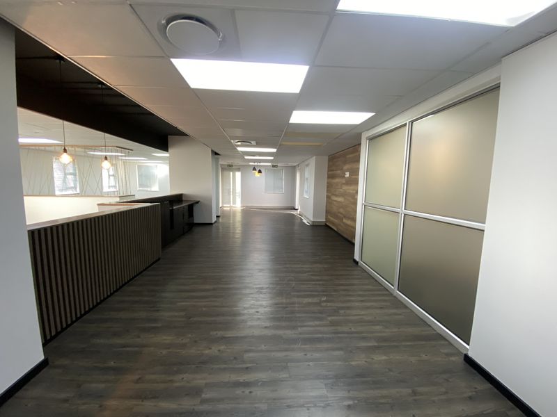 Spacious open-plan office area featuring modern laminate flooring, a wood-paneled feature wall, and frosted glass partitions, offering a clean and professional workspace.