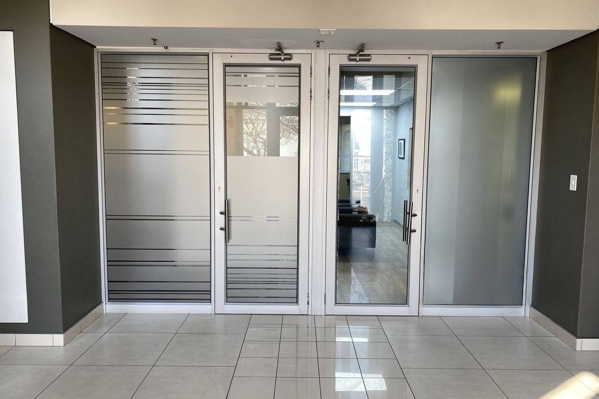 A modern office entrance featuring glass double doors with frosted detailing and polished ceramic floor tiles.