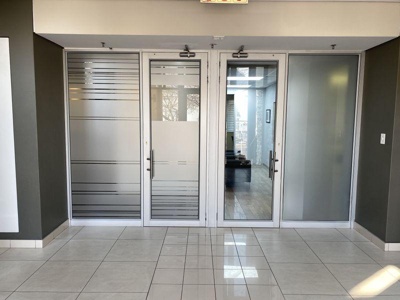 A modern office entrance featuring glass double doors with frosted detailing and polished ceramic floor tiles.