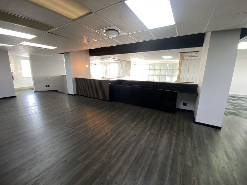 Spacious open-plan office area featuring modern laminate flooring, a suspended ceiling with recessed lighting, and a sleek built-in kitchenette counter.
