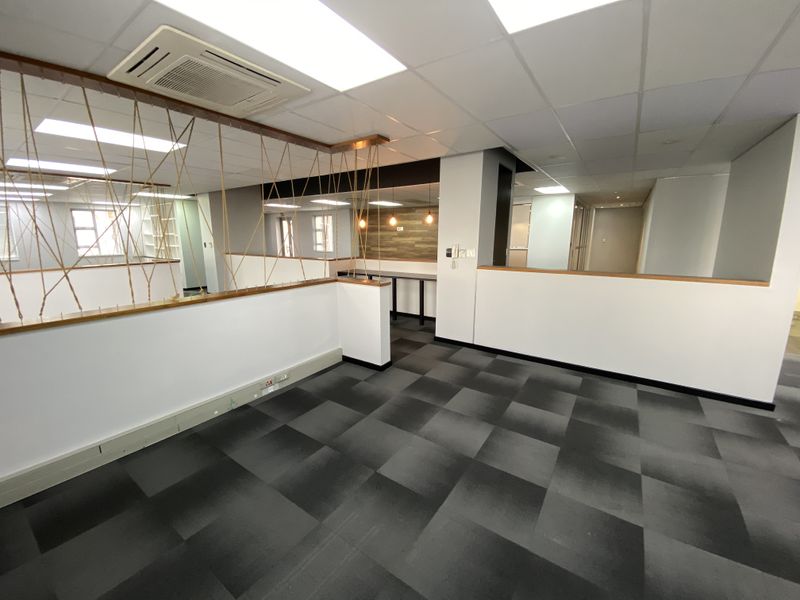 Modern open-plan office space featuring carpet tiles, suspended ceilings with recessed lighting, integrated air conditioning, and a decorative timber partition.