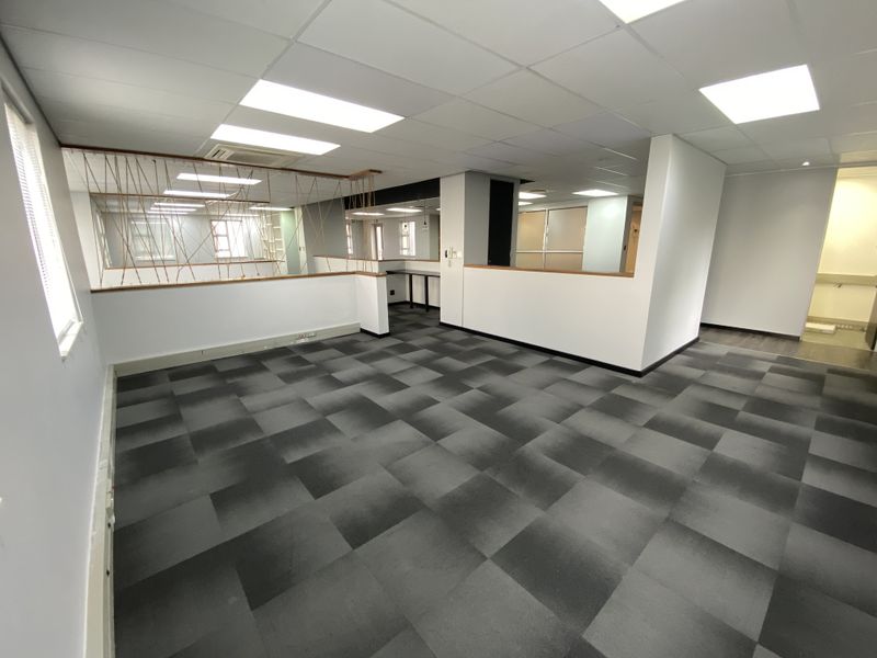 A spacious, open-plan office area featuring modern carpet tiles, suspended ceilings with recessed lighting, and clean, neutral partition walls.