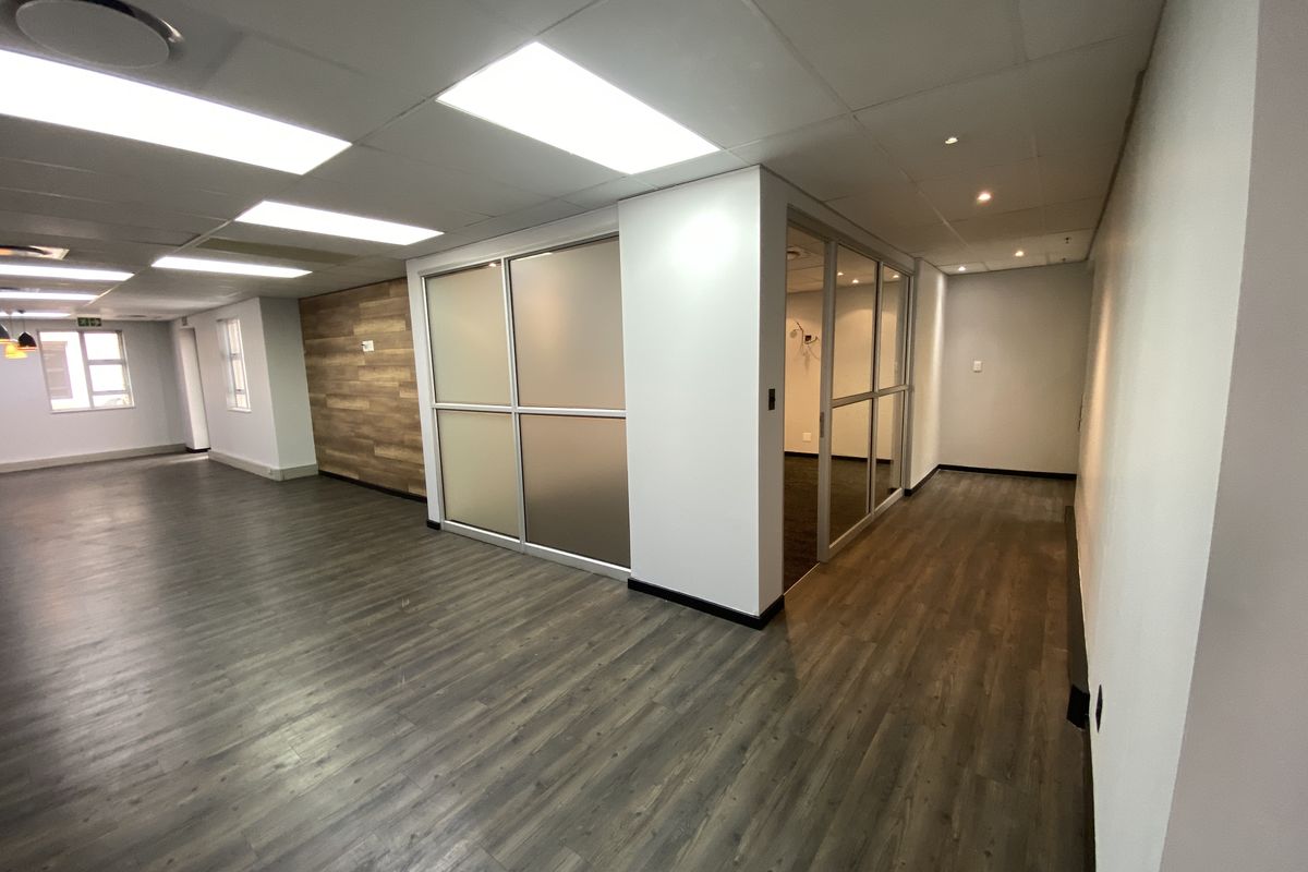 Modern open-plan office space featuring laminate flooring, recessed lighting, glass partitions, and a stylish wood-paneled feature wall.