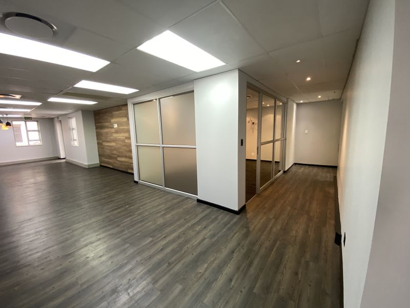Modern open-plan office space featuring laminate flooring, recessed lighting, glass partitions, and a stylish wood-paneled feature wall.