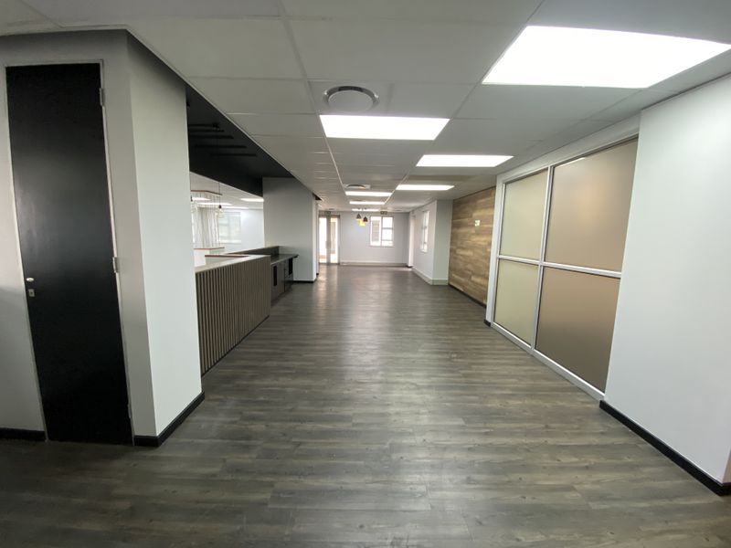 A modern, open-plan office space featuring laminate flooring, a suspended ceiling with recessed lighting, and contemporary frosted glass partitions.