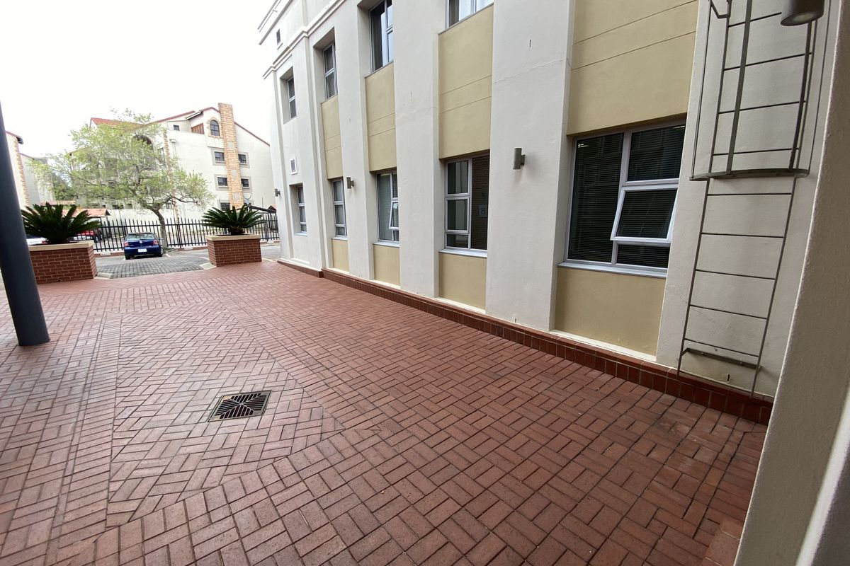 A paved rear exterior area of the office building featuring a fire escape ladder, drainage, and well-maintained brickwork.