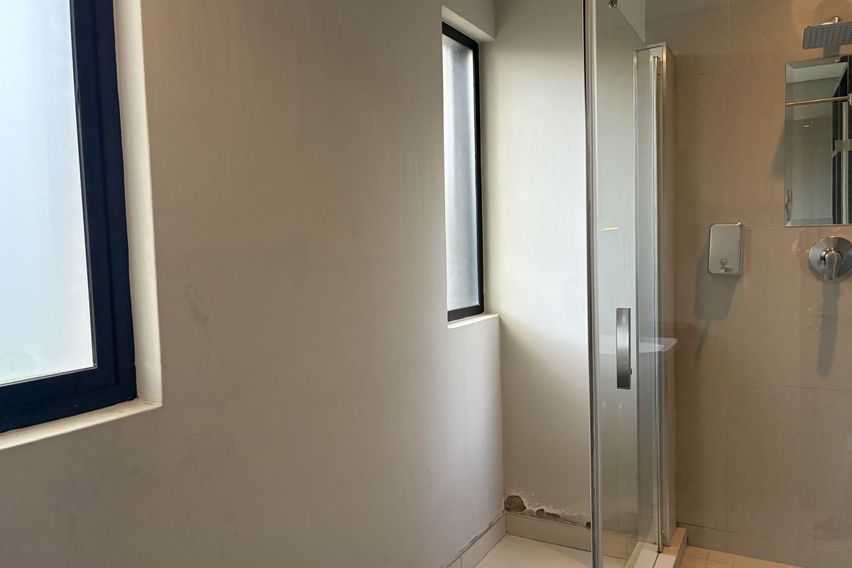 A functional bathroom featuring a glass-enclosed shower, tiled finishes, and natural light from windows, requiring minor cosmetic repairs to the wall plaster.