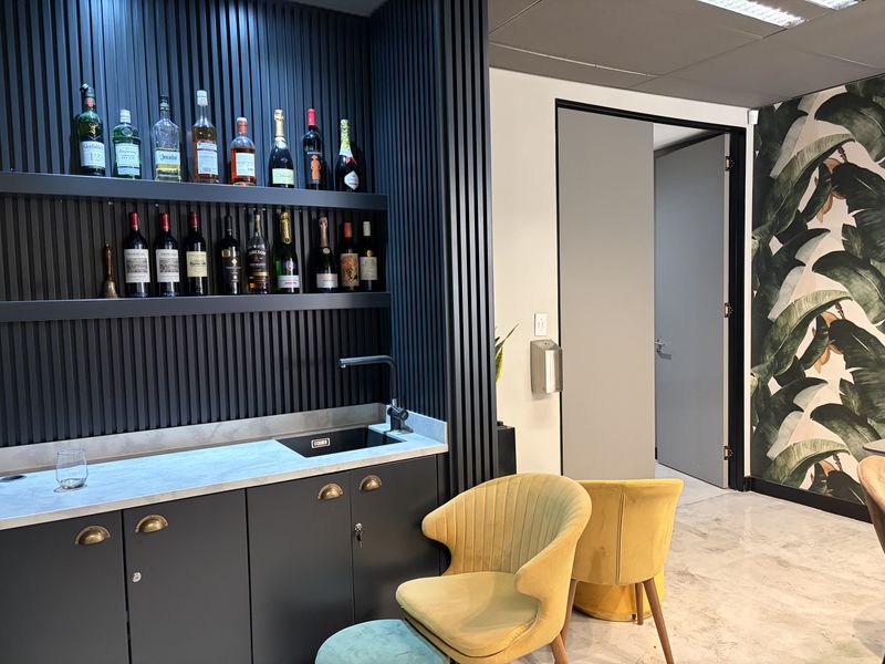 A modern, well-appointed bar area featuring dark slatted wall paneling, built-in cabinetry with stone countertops, and an integrated sink.
