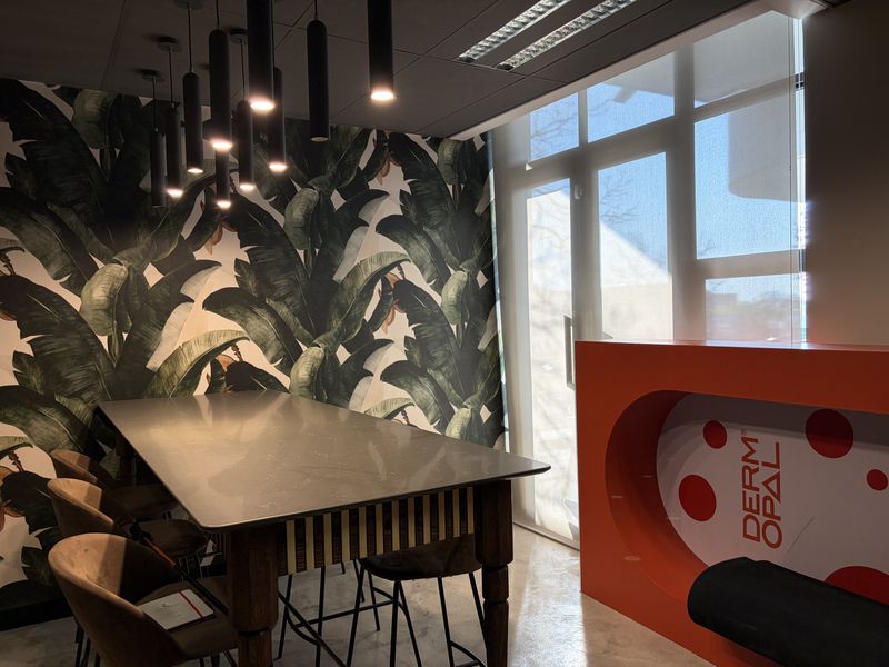Modern office space featuring a large table, decorative wallpaper, pendant lighting, and a built-in reception desk with natural light from a large window.