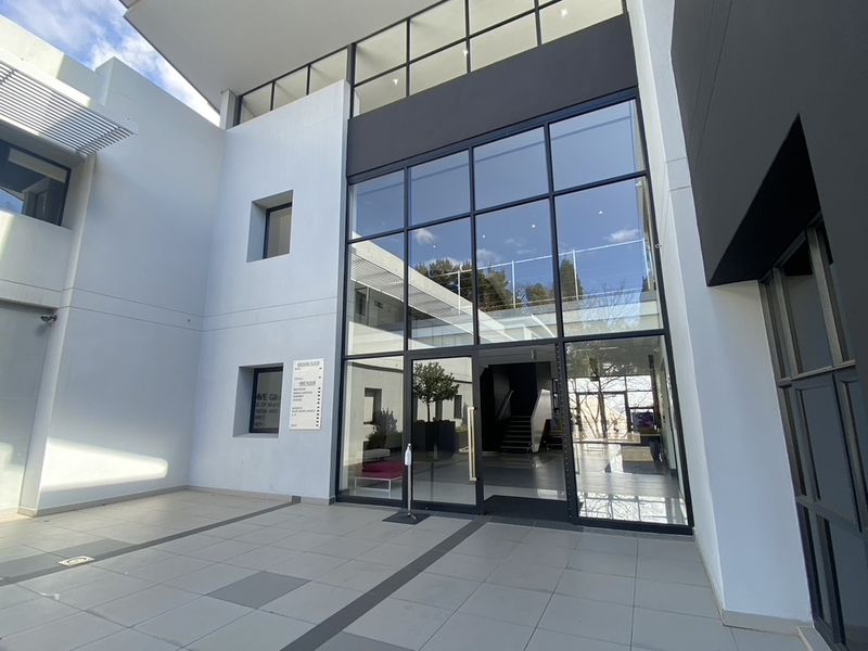 Modern commercial building entrance featuring a large glass facade, tiled courtyard, and clear directory signage for professional office access.