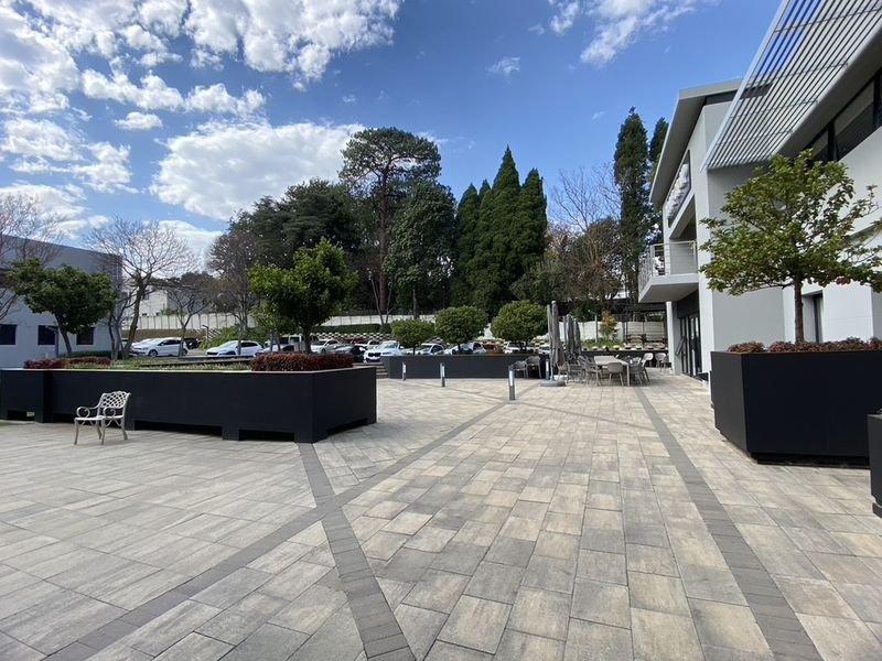 A well-maintained commercial outdoor terrace featuring paved flooring, integrated modern planters, and architectural shading elements, providing a professional exterior space.