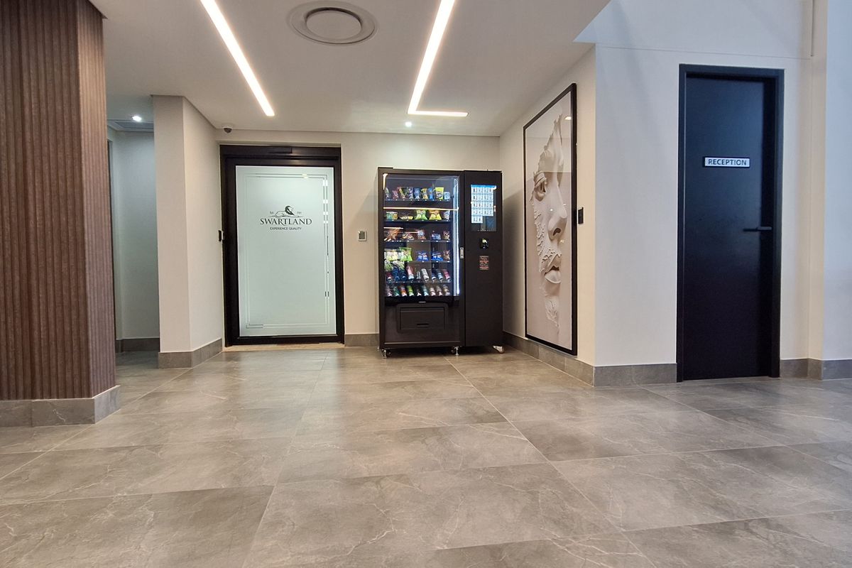 Modern office building entrance lobby featuring tiled flooring, recessed linear lighting, and a secure access turnstile.