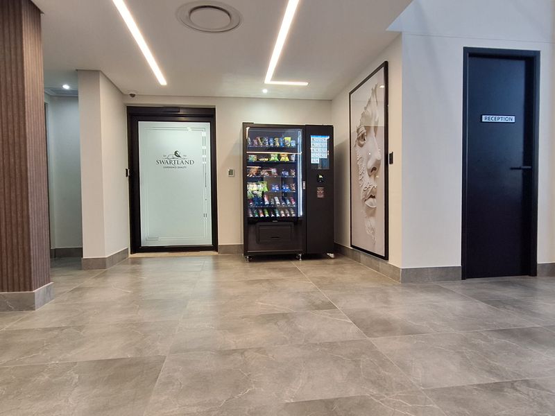 Modern office building entrance lobby featuring tiled flooring, recessed linear lighting, and a secure access turnstile.