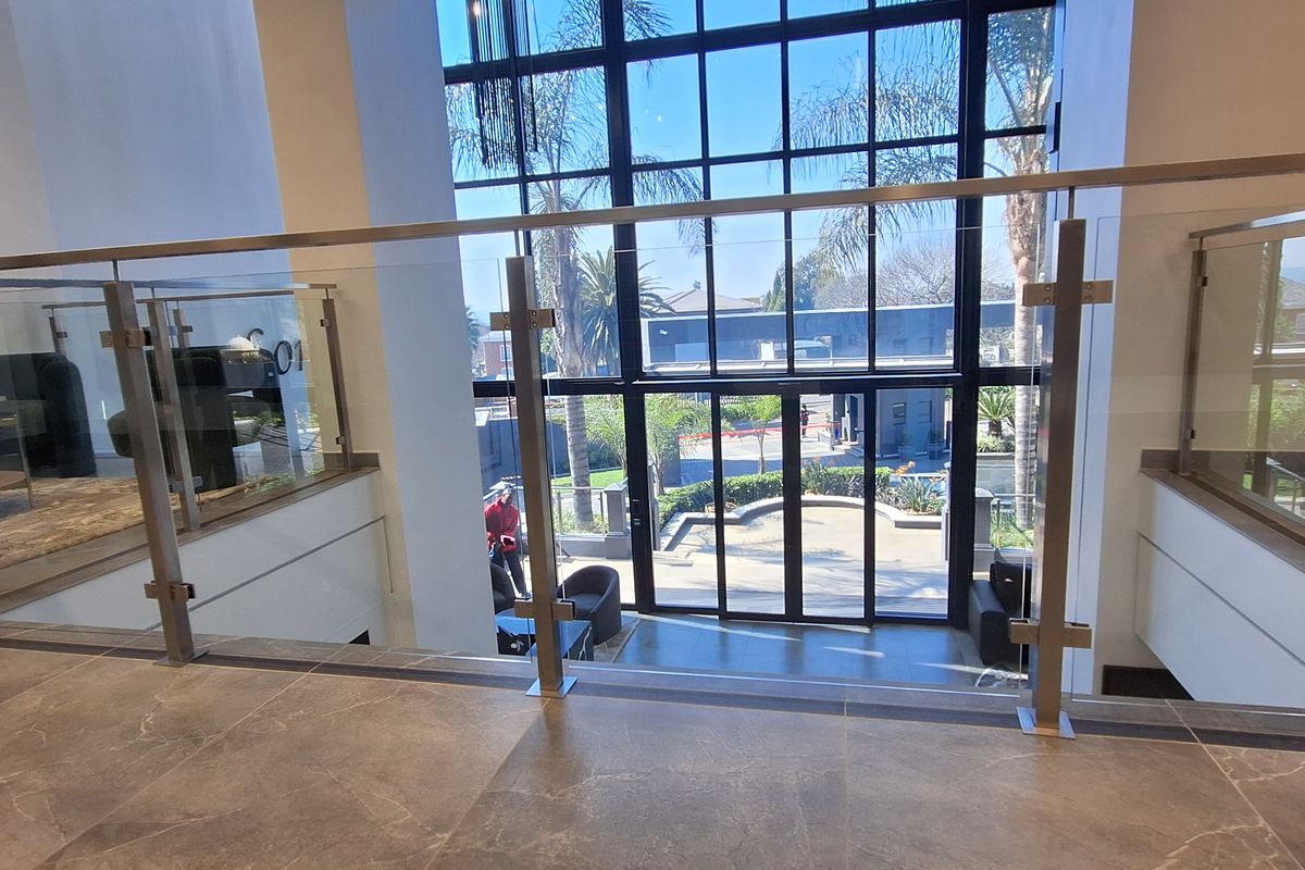 Modern double-volume office entrance featuring large format floor tiles, a sleek glass balustrade, and expansive floor-to-ceiling windows providing natural light.