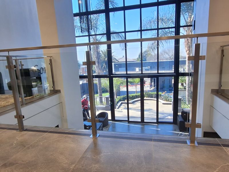 Modern double-volume office entrance featuring large format floor tiles, a sleek glass balustrade, and expansive floor-to-ceiling windows providing natural light.