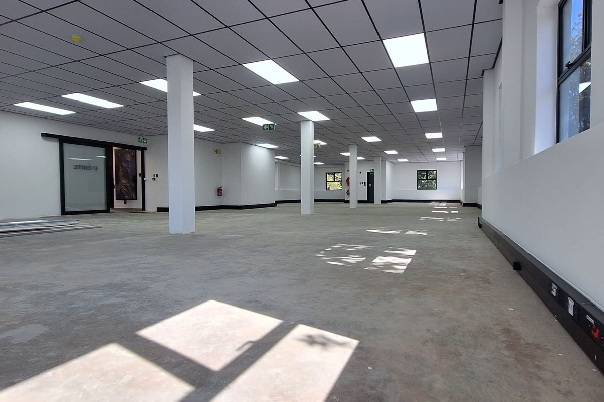Spacious open-plan office area featuring a suspended ceiling, recessed lighting, structural columns, and perimeter trunking for electrical and data connectivity.