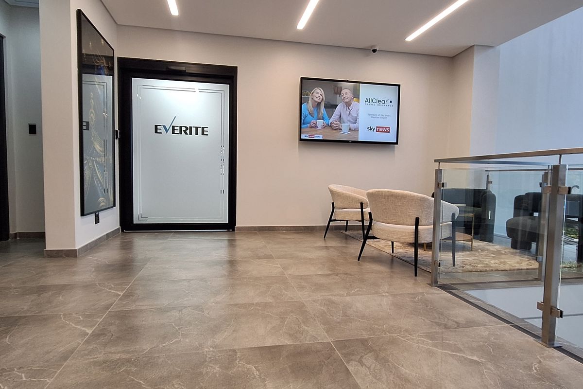 Modern office reception area featuring tiled flooring, recessed linear lighting, and a glass balustrade overlooking the lower level.