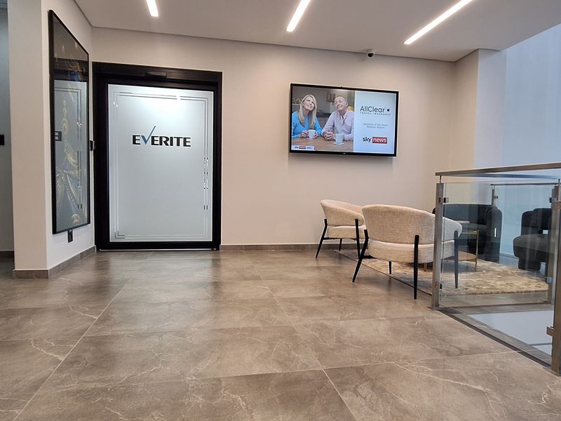 Modern office reception area featuring tiled flooring, recessed linear lighting, and a glass balustrade overlooking the lower level.