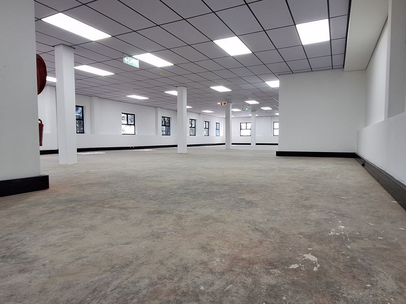 A large, open-plan office space featuring a suspended ceiling, recessed lighting, and structural columns, currently awaiting flooring installation and final finishes.