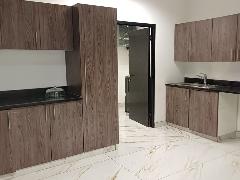 Modern office kitchenette featuring wood-grain cabinetry, black stone countertops, stainless steel sink, and elegant marble-look floor tiles.