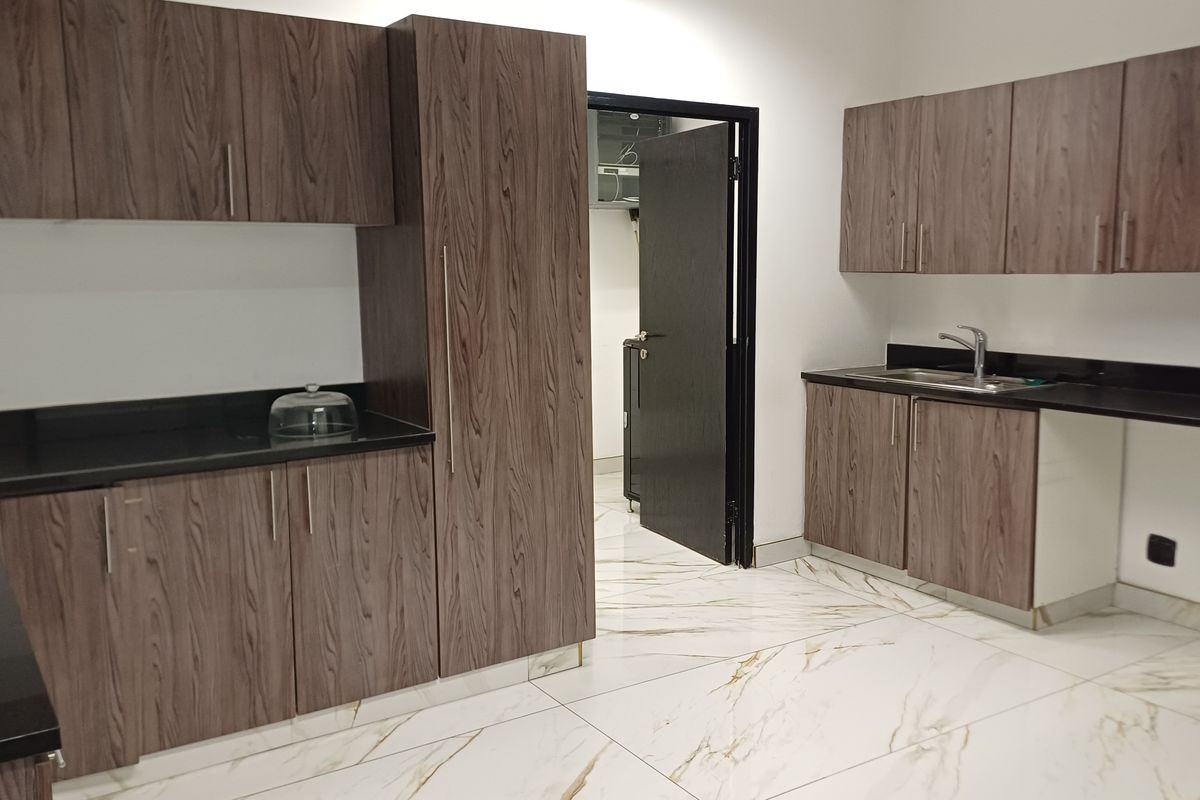 Modern office kitchenette featuring wood-grain cabinetry, black stone countertops, stainless steel sink, and elegant marble-look floor tiles.