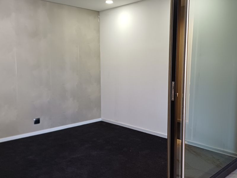 A modern, empty office space featuring a textured feature wall, dark carpet flooring, and a sleek glass partition wall with recessed lighting.