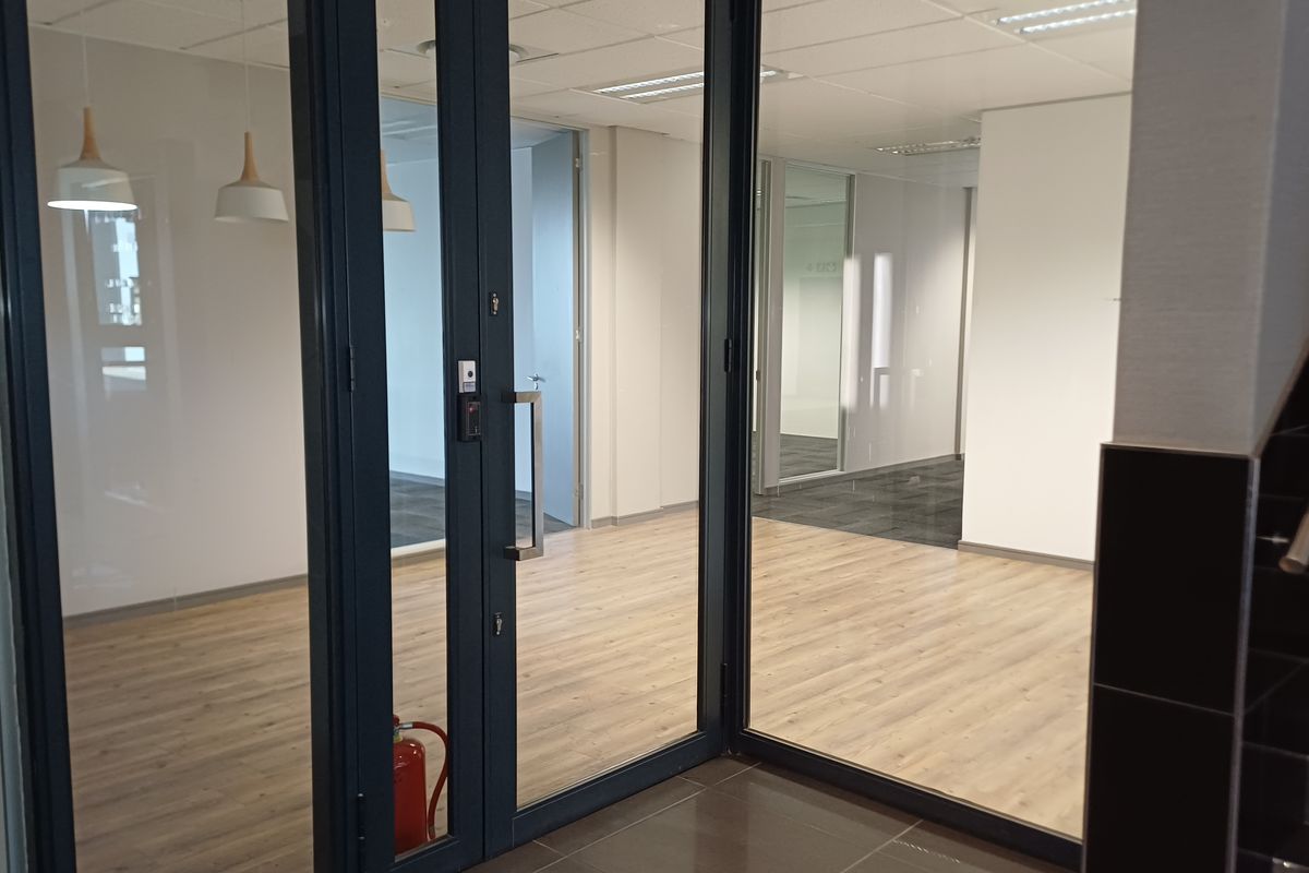 Modern open-plan office space featuring glass partitions, laminate flooring, and a suspended ceiling with recessed lighting.