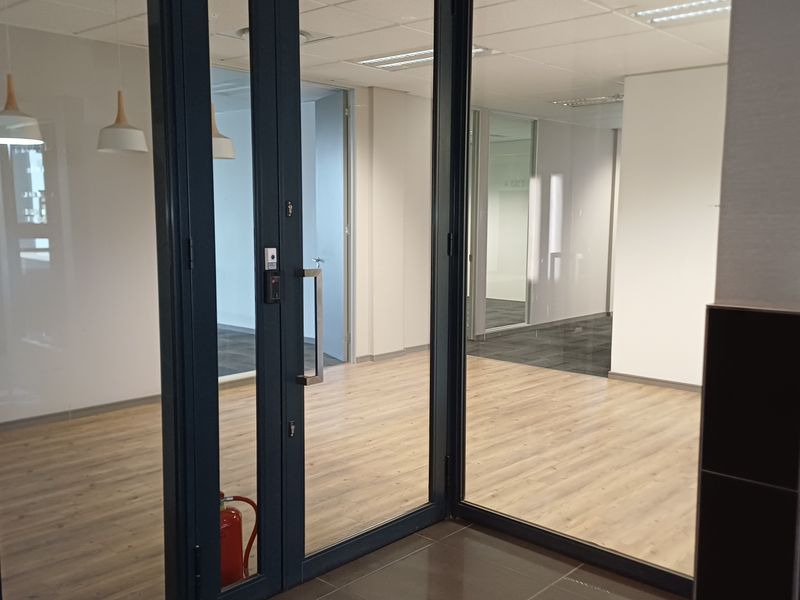 Modern open-plan office space featuring glass partitions, laminate flooring, and a suspended ceiling with recessed lighting.