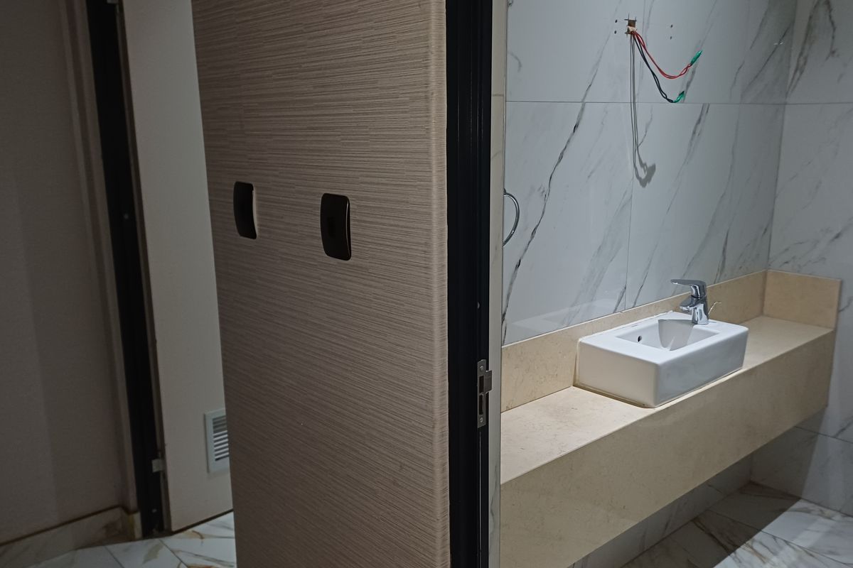 A modern bathroom featuring marble-effect wall tiles, a stone vanity countertop with a basin, and a toilet, currently awaiting final electrical fixture installation.