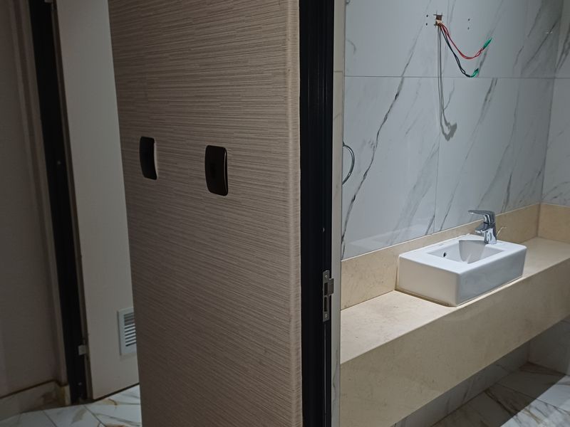 A modern bathroom featuring marble-effect wall tiles, a stone vanity countertop with a basin, and a toilet, currently awaiting final electrical fixture installation.