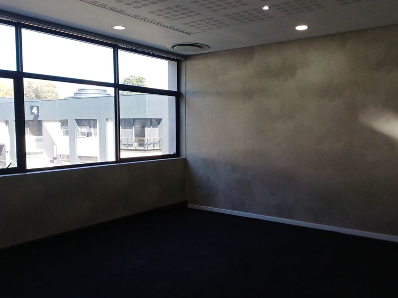 A bright, empty office space featuring large windows, modern recessed lighting, ducted air conditioning, and a textured feature wall.
