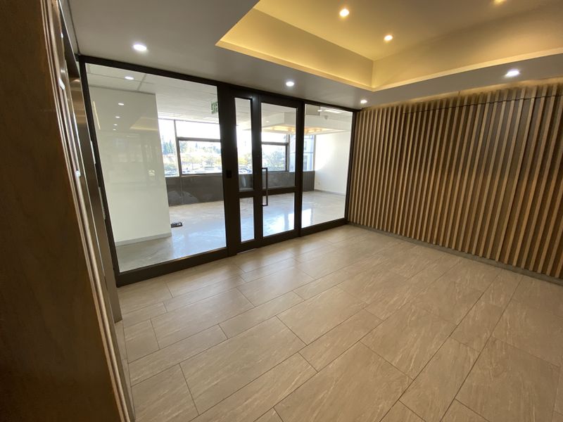 Modern office lobby or reception area featuring contemporary timber slat wall paneling, glass partitions, and high-quality tiled flooring with recessed ceiling lighting.