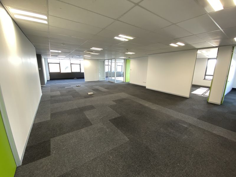 Spacious open-plan office area featuring carpeted flooring, suspended ceilings with recessed lighting, and glass partitioning for a modern, professional workspace.