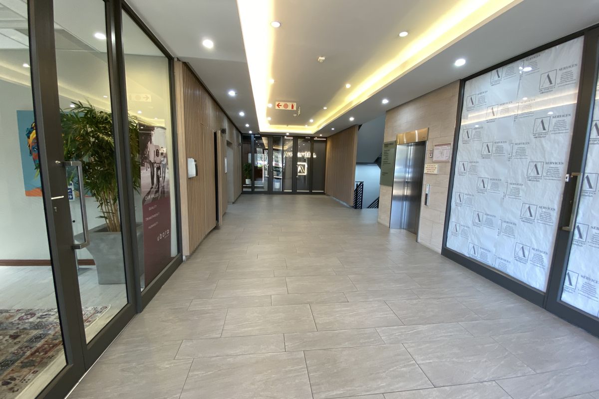 Modern office building lobby or hallway featuring tiled flooring, recessed cove lighting, timber slat wall accents, and elevator access.