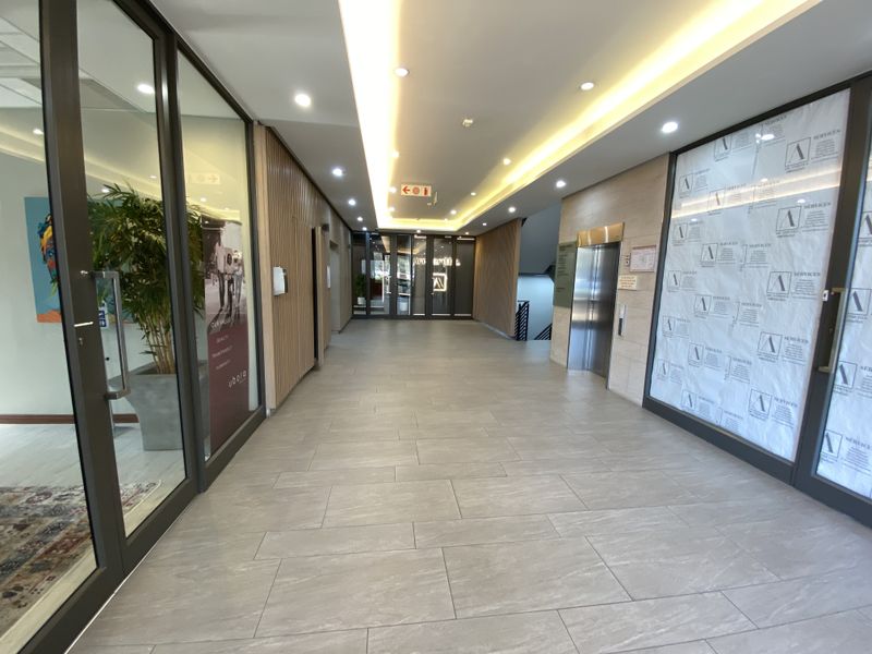 Modern office building lobby or hallway featuring tiled flooring, recessed cove lighting, timber slat wall accents, and elevator access.