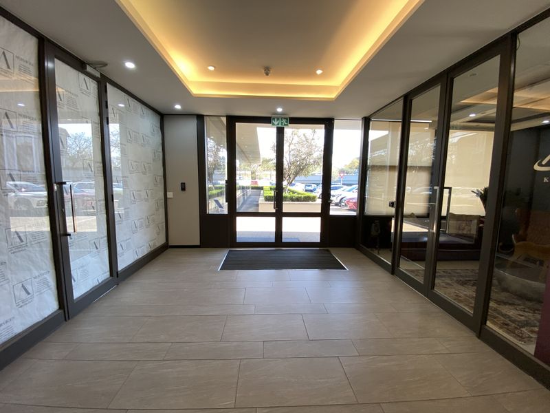 Modern office building entrance lobby featuring tiled flooring, recessed ceiling lighting, and glass partition walls providing a bright and professional welcome area.