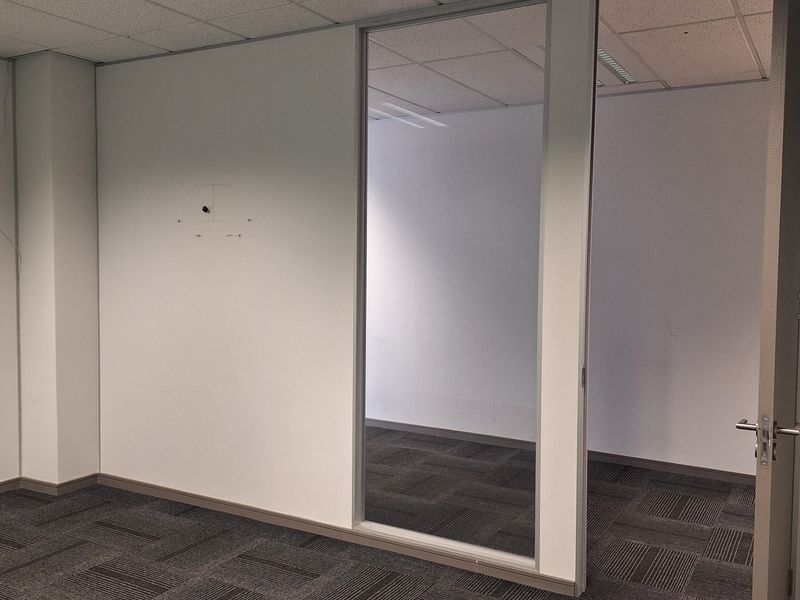 An empty office space featuring a glass partition, suspended ceiling, and dark patterned carpet tiles.