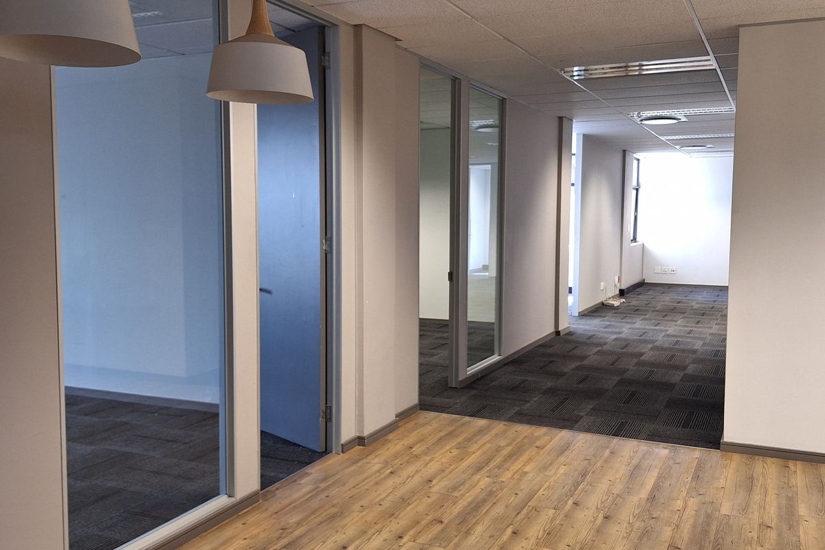 Modern office space featuring a mix of wood-look vinyl and carpet flooring, glass partitions, and suspended ceilings with recessed lighting.