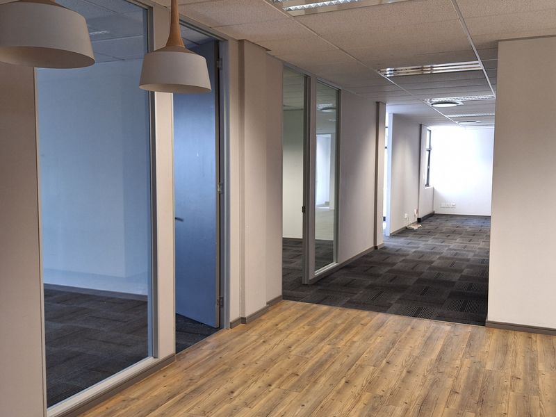Modern office space featuring a mix of wood-look vinyl and carpet flooring, glass partitions, and suspended ceilings with recessed lighting.