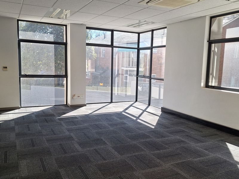 A bright, empty office space featuring large windows, carpet tiles, and a suspended ceiling with integrated air conditioning.