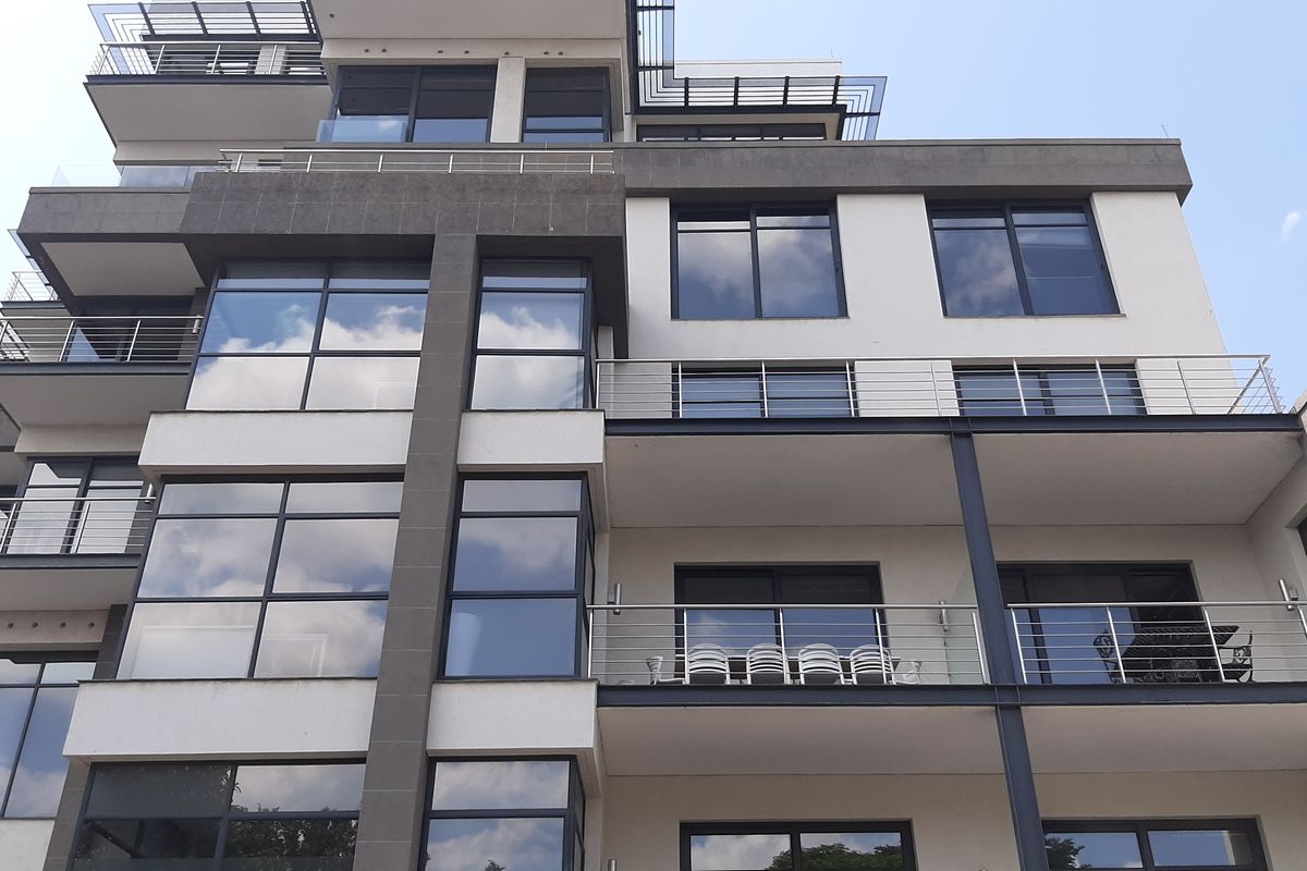 A modern multi-story office building facade featuring extensive glass windows and stainless steel balcony railings across multiple levels.