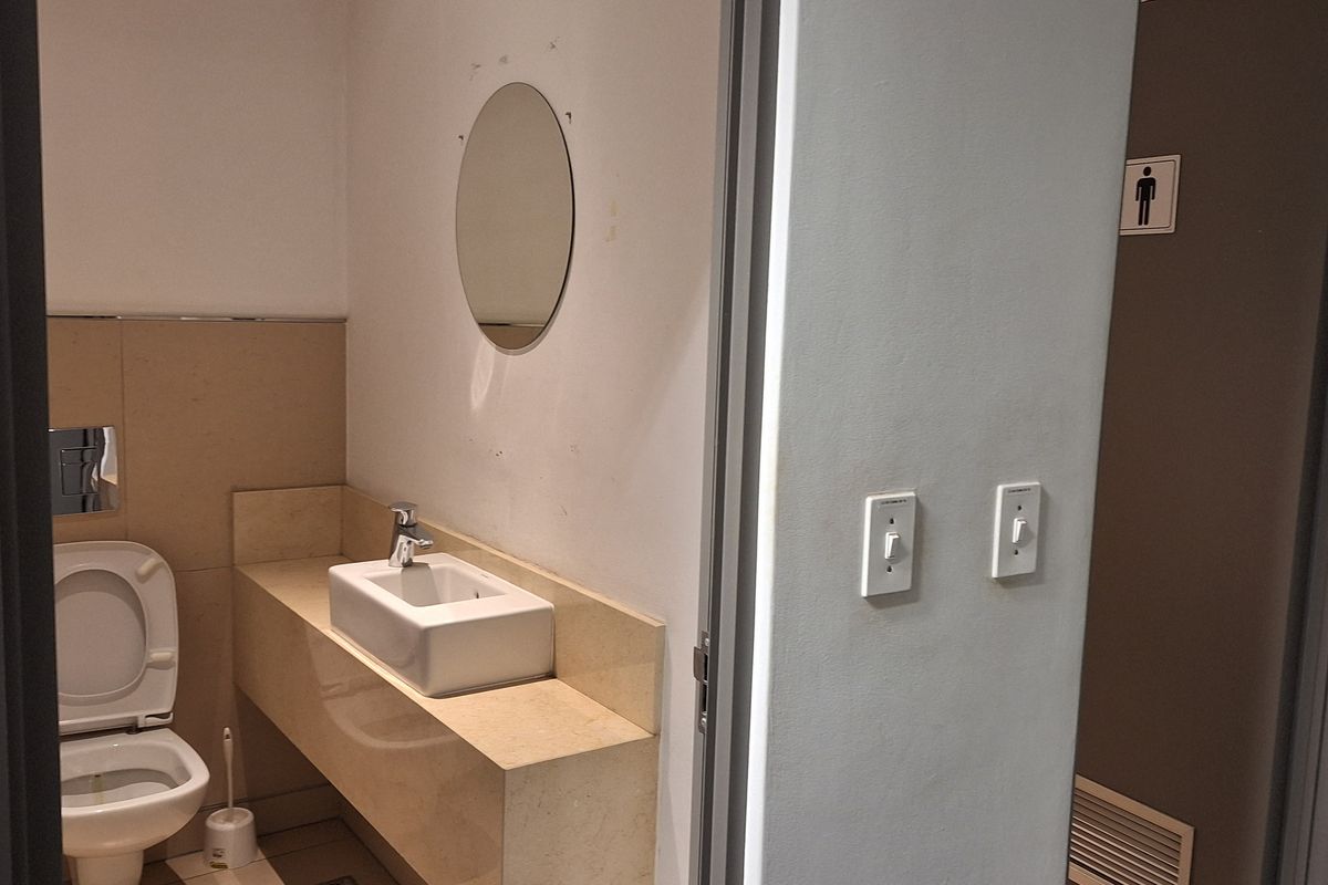 A functional office restroom featuring a wall-mounted toilet, floating vanity with a vessel sink, and neutral tile finishes.