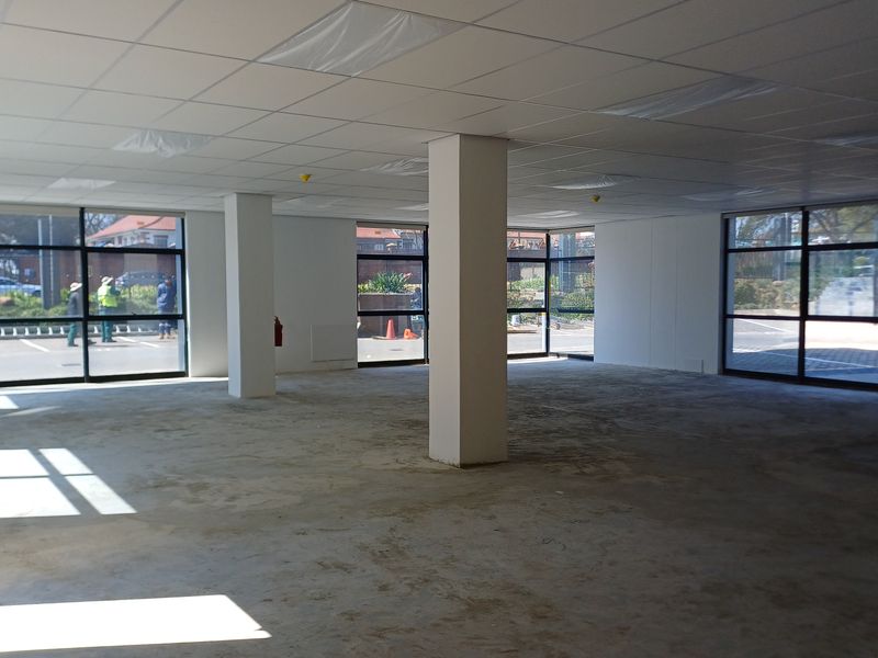 An open-plan office space featuring large windows, structural columns, and a suspended ceiling, currently in a shell condition awaiting final flooring and finishes.