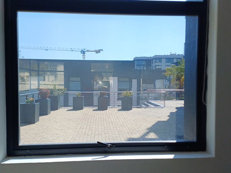 A view from an office window looking out onto a paved terrace area with metal railings and surrounding urban buildings.