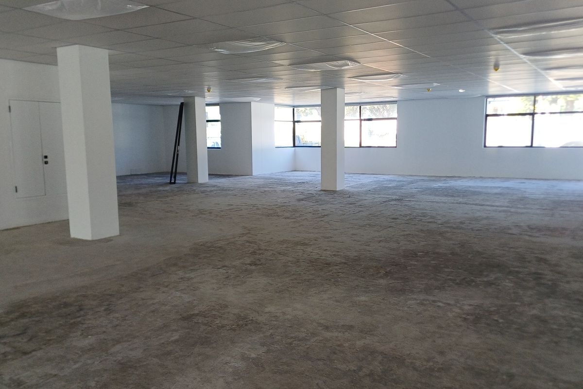 A large, open-plan office space featuring a suspended ceiling, structural columns, and expansive windows, currently awaiting final flooring installation.